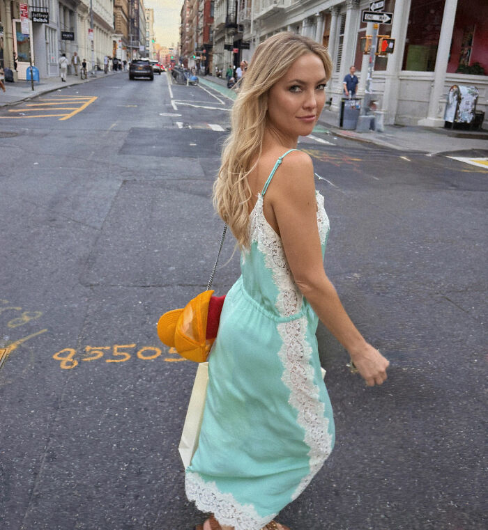 Kate Hudson wearing a mint green dress with white lace detail, walking on a city street with a casual pose.