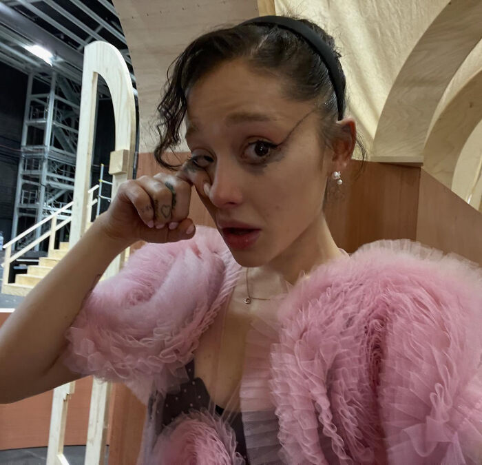 Young woman in a pink ruffled dress wiping tears, conveying emotional struggles related to Ariana Grande's family and singer challenges. Young woman in a pink ruffled dress wiping tears, conveying emotional struggles related to Ariana Grande's family and singer challenges.