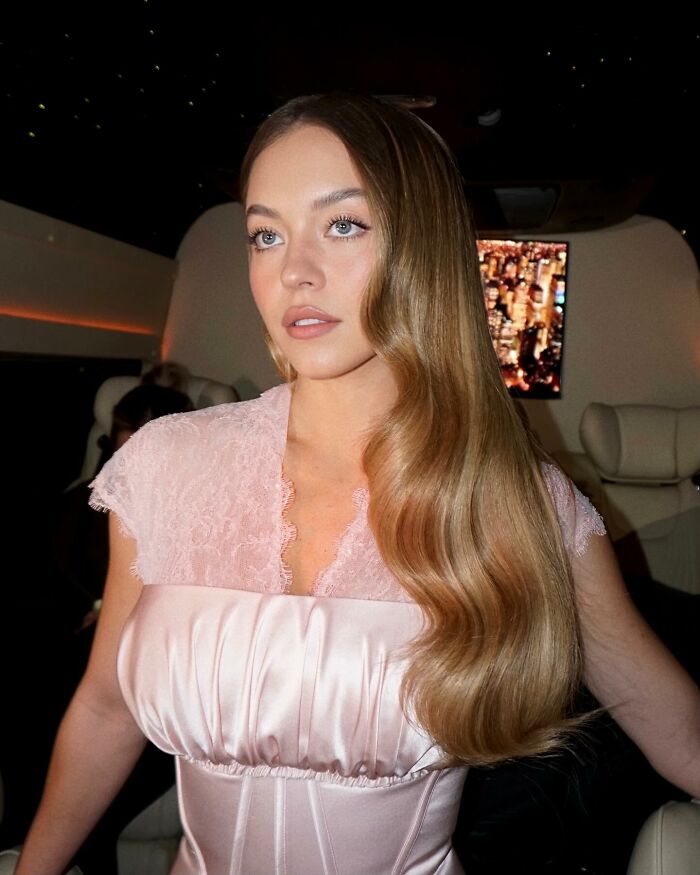 Sydney Sweeney with long wavy hair and soft makeup in a pink satin dress, highlighting her viral MAGA makeover look. Sydney Sweeney with long wavy hair and soft makeup in a pink satin dress, highlighting her viral MAGA makeover look.