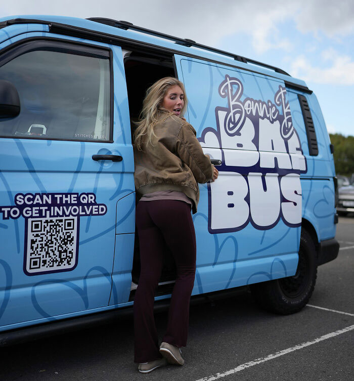 Woman standing by a blue Bonnie Blue bus with QR code, symbolizing Bonnie Blue learning her fate after controversial video arrest. Woman standing by a blue Bonnie Blue bus with QR code, symbolizing Bonnie Blue learning her fate after controversial video arrest.