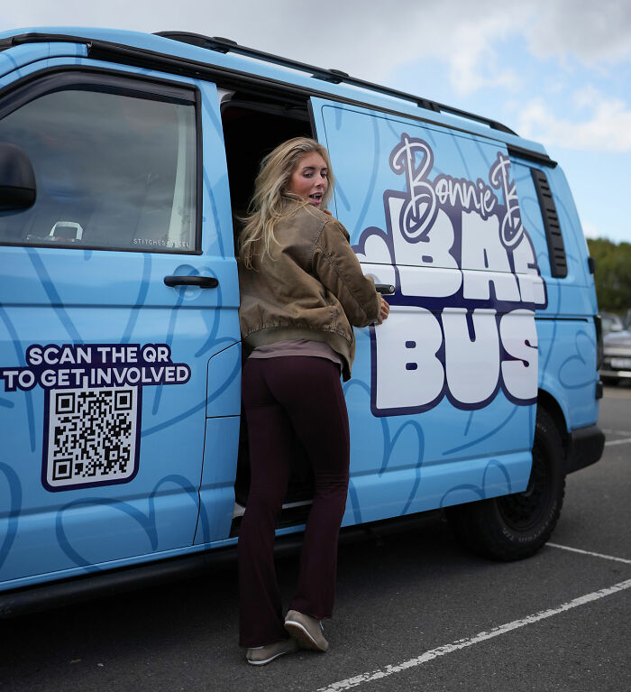 Woman standing by blue Bonnie Blue bus with QR code on door, related to Bonnie Blue faces 15-year sentence news.