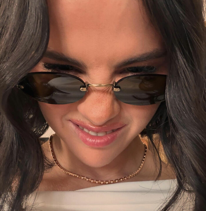 Selena Gomez smiling, wearing sunglasses and a gold chain necklace in a close-up photo. Selena Gomez smiling, wearing sunglasses and a gold chain necklace in a close-up photo.