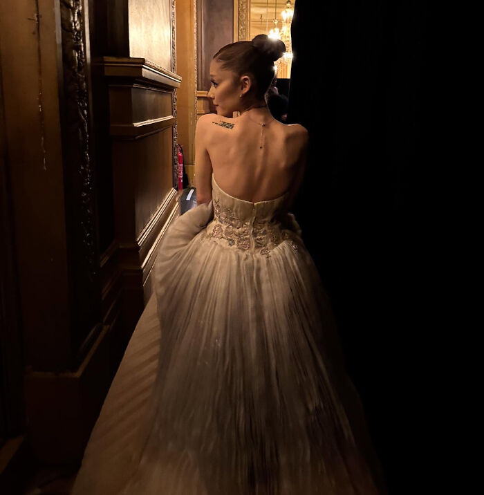 Ariana Grande in a strapless gown, backstage in dim lighting, highlighting struggles shared by family member. Ariana Grande in a strapless gown, backstage in dim lighting, highlighting struggles shared by family member.