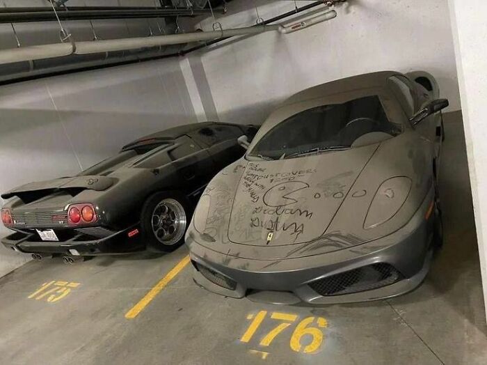 Two luxury sports cars in a parking garage, one covered in dust with trippy drawings on the hood.