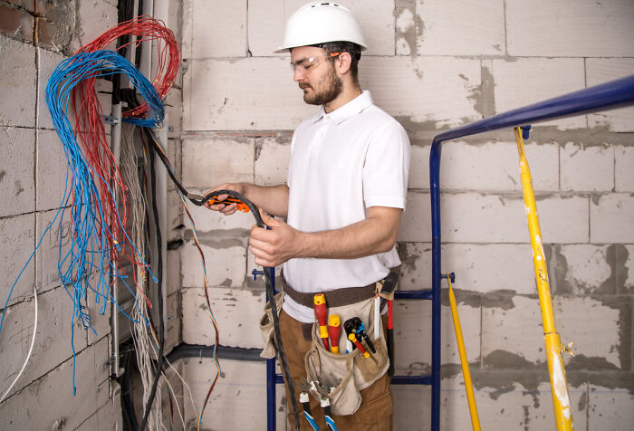 Man wearing a hard hat working with electrical wires in a construction site, illustrating signs of high school era influence.