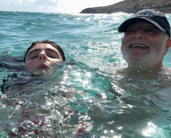 Rob Reiner's daughter and father swimming in ocean waves under clear sky near rocky coastline. Rob Reiner's daughter and father swimming in ocean waves under clear sky near rocky coastline.