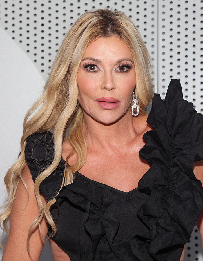 Brandi Glanville wearing a black ruffle dress and statement earrings posing against a dotted white background. Brandi Glanville wearing a black ruffle dress and statement earrings posing against a dotted white background.