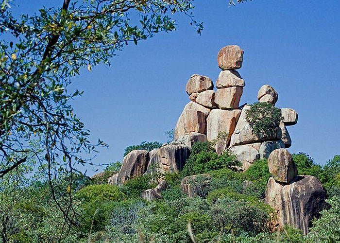 Natural rock formations that look AI generated but are actually real, surrounded by greenery under a clear blue sky.