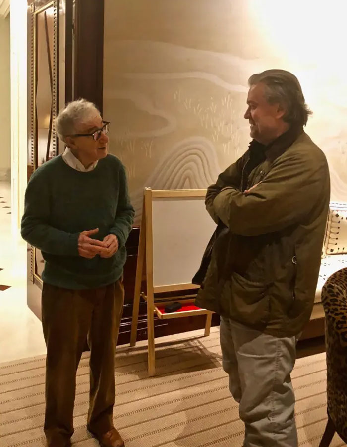 Two men conversing indoors near a wooden easel, with a focus on disturbing Epstein desk photo after estate images release.