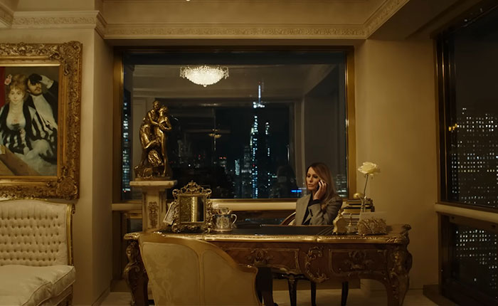 Melania Trump sitting at an ornate desk in a luxurious room with city skyline visible through large windows at night Melania Trump sitting at an ornate desk in a luxurious room with city skyline visible through large windows at night