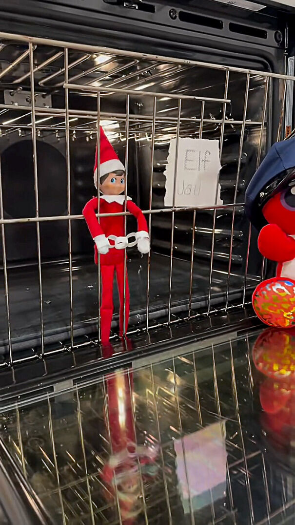 Elf on the Shelf dressed in red with paper chains behind oven bars labeled Elf Jail in a mischievous holiday setup
