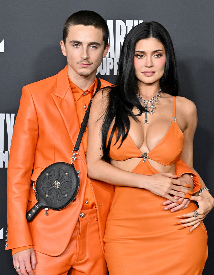 Timothée Chalamet wearing orange suit posing with woman in orange dress at an event, highlighting arrogance controversy. Timothée Chalamet wearing orange suit posing with woman in orange dress at an event, highlighting arrogance controversy.