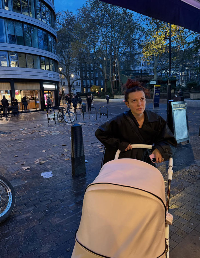 Millie Bobby Brown pushing a stroller outdoors at dusk, showing an arm injury that fuels fan theories about Jake Bongiovi control. Millie Bobby Brown pushing a stroller outdoors at dusk, showing an arm injury that fuels fan theories about Jake Bongiovi control.