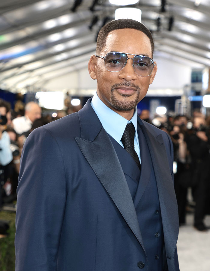 Actor wearing blue suit and glasses at event, illustrating outrageous demands actors have allegedly made in contracts.