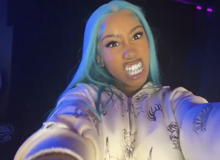 North West, 12, with blue hair and grills, posing with a fierce expression in a dimly lit setting.