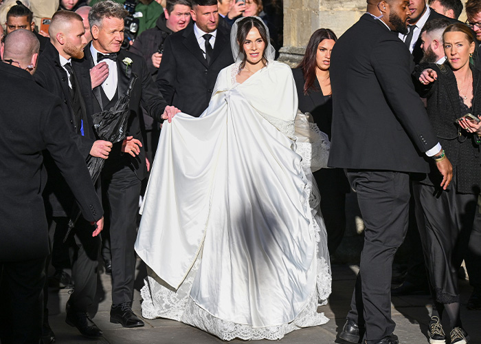 Bride in a white satin bed sheet style wedding dress surrounded by guests at an outdoor event. Bride in a white satin bed sheet style wedding dress surrounded by guests at an outdoor event.