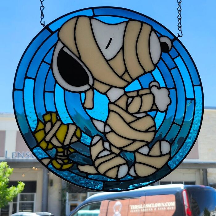 Stained glass sign featuring pop culture icon Snoopy wrapped as a mummy in vivid blue and beige hues.