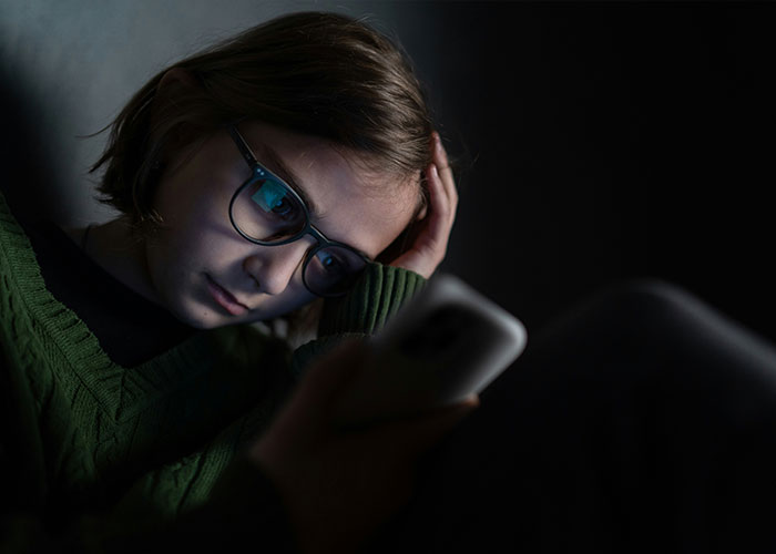 Teenage girl wearing glasses looks distressed while using a smartphone in a dark room, highlighting ChatGPT controversy. Teenage girl wearing glasses looks distressed while using a smartphone in a dark room, highlighting ChatGPT controversy.