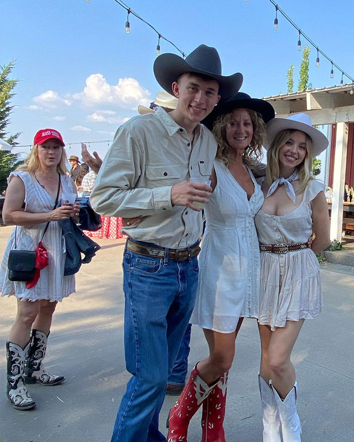 Group of people at an outdoor event wearing cowboy hats and boots, capturing Sydney Sweeney and Lindsay Lohan comparison reactions.