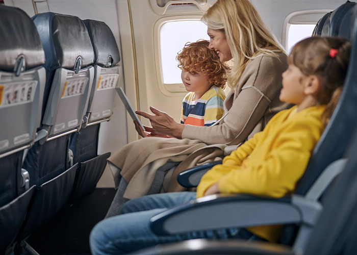 Woman and children sitting on airplane seats engaged with a tablet during a flight, highlighting internet divided discussion.