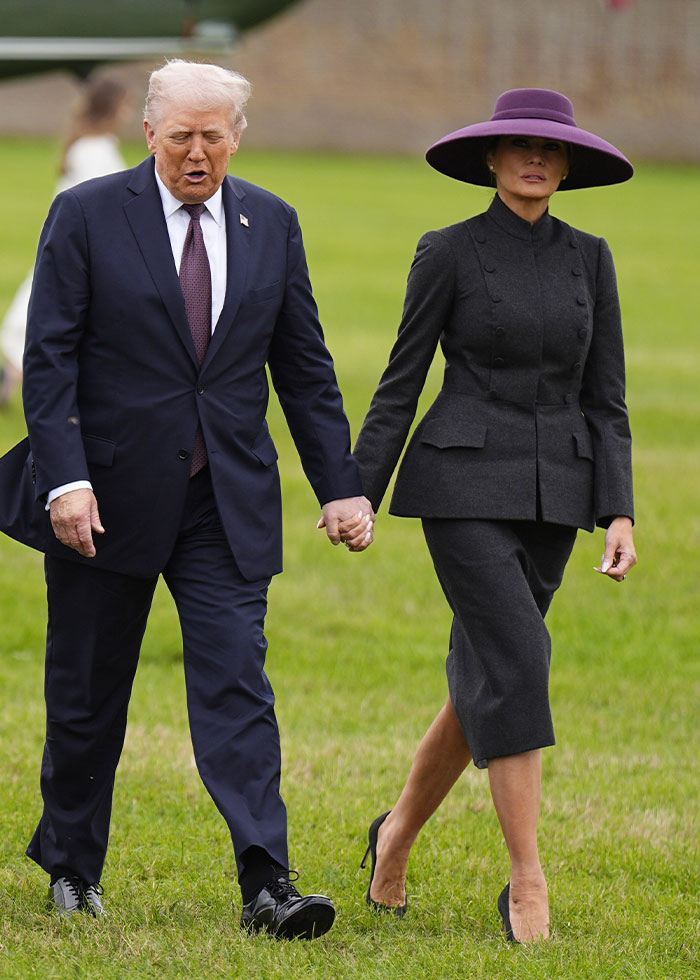 Man in navy suit holding hands with woman in dark gray outfit and large purple hat, showcasing celebrity fashion disasters 2025.