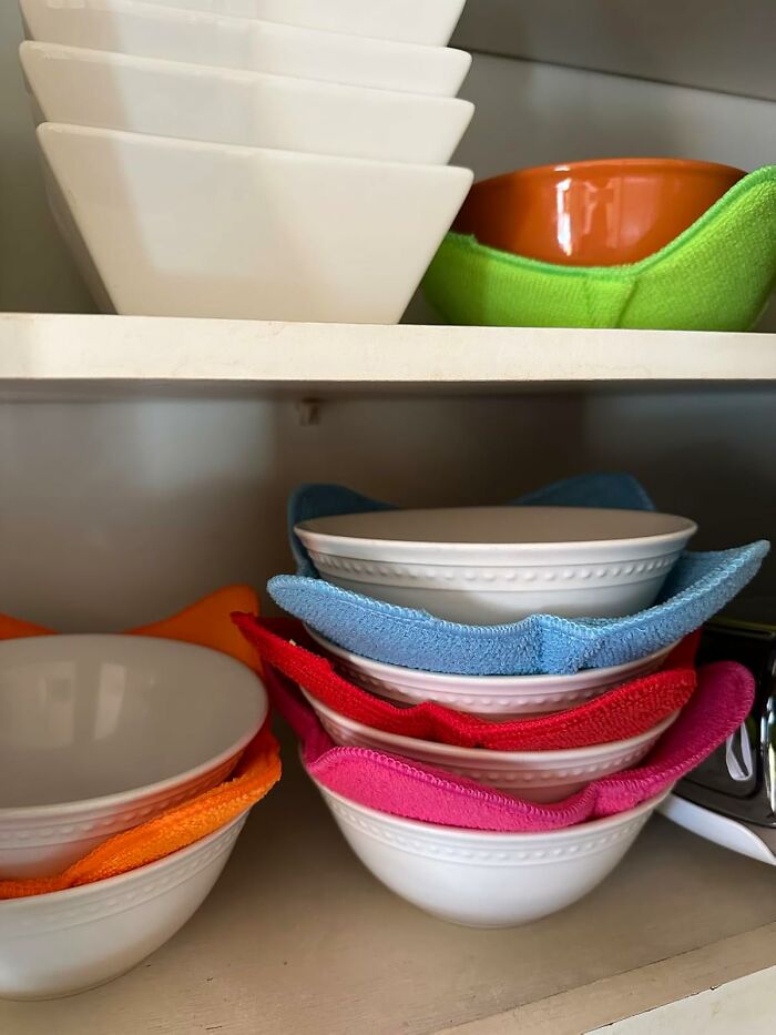 Stacked white bowls with colorful microfiber cloths in a kitchen cabinet as a useful present idea for favorite child gifts.