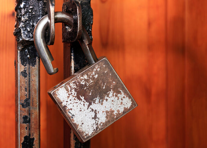 Rusty open padlock hanging on worn metal gate symbolizing unresolved mysteries that still give people chills.