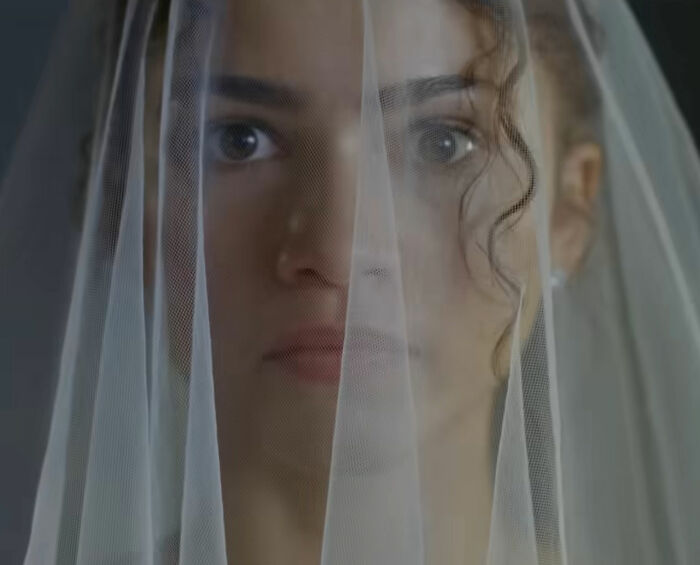 Zendaya wearing a bridal veil, looking through sheer fabric in viral engagement ad related to Robert Pattinson.