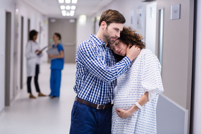Man comforting pregnant woman in hospital hallway, illustrating men missed delivery babies and emotional support.