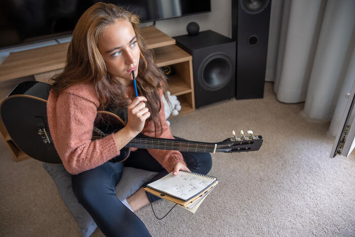 Young woman holding guitar and notebook, deep in thought about crazy things ex will always pine for her.