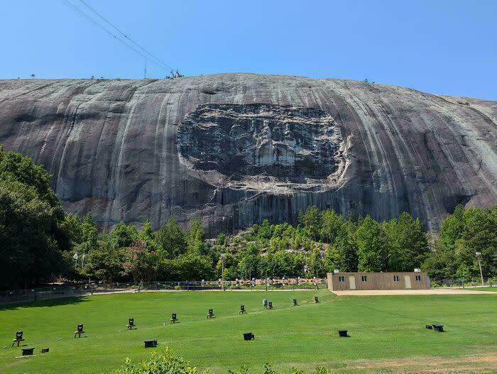 Massive rock face with a carved monument, surrounded by greenery and clear blue sky, evoking megalophobia fears.
