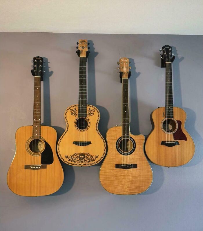 Four acoustic guitars perfectly aligned side by side against a gray wall showcasing intricate wood patterns and designs.