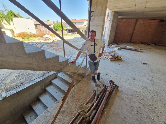Man standing next to poorly constructed concrete stairs in an unfinished building showing job done poorly