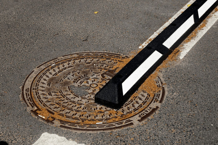 A road barrier awkwardly installed on top of a manhole cover, showing a poor job and construction fail.