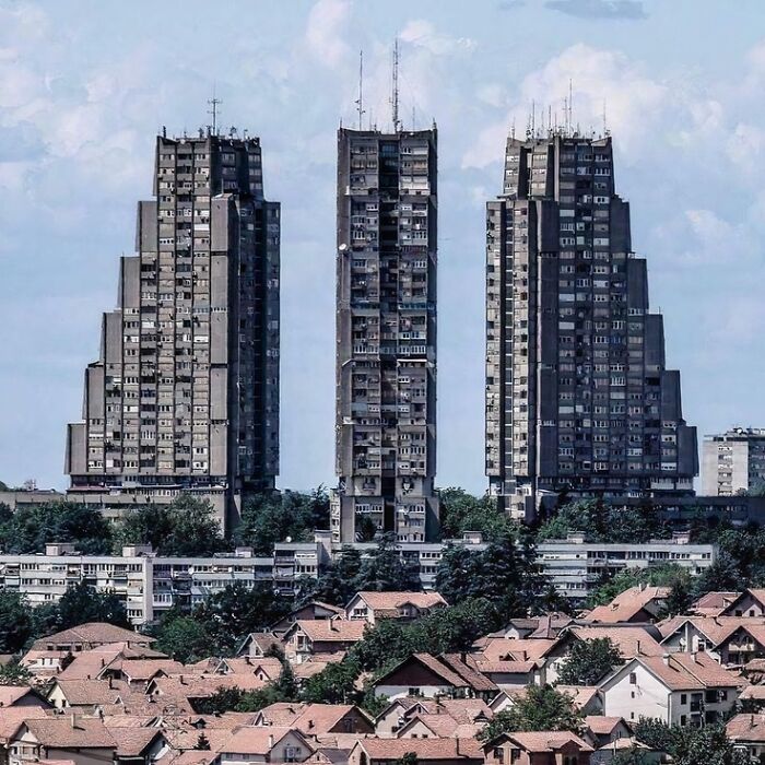 Three imposing buildings with brutalist architecture towering over a residential neighborhood, appearing like evil buildings.