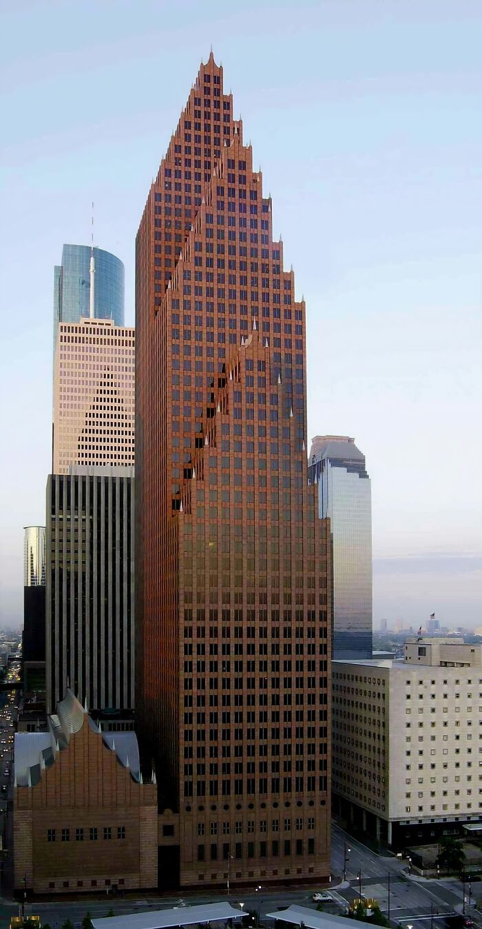 Tall evil building with sharp, stepped architecture standing among other skyscrapers in an urban cityscape at dusk