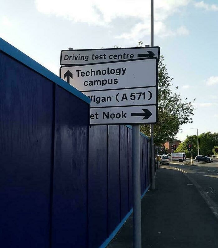 Road signs with confusing directions partially obscured by a fence, showing poor job e*******n in public signage placement.