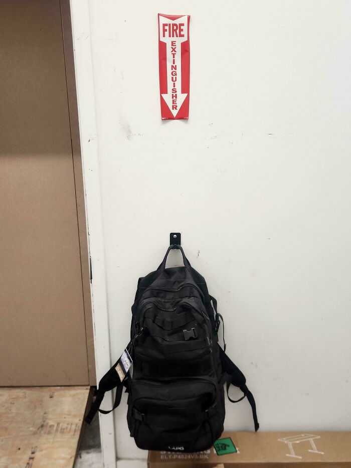 Backpack hanging on a wall under a fire extinguisher sign, demonstrating poor job placement and workplace safety.