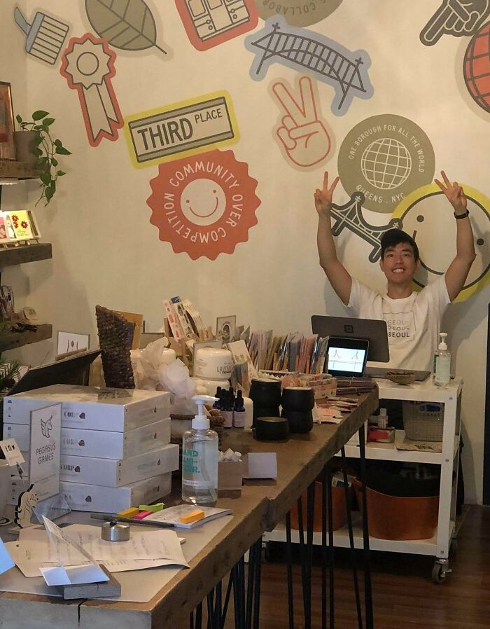 Young entrepreneur celebrating success in a cozy shop, surrounded by products and community over competition wall art.