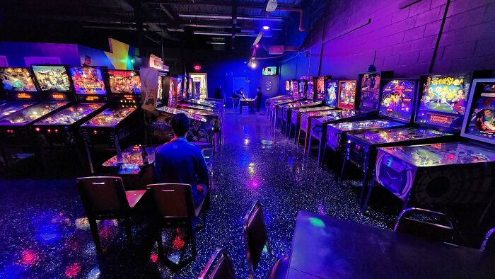 Person sitting alone in a colorful arcade filled with pinball machines, capturing a moment of leap of faith decisions.