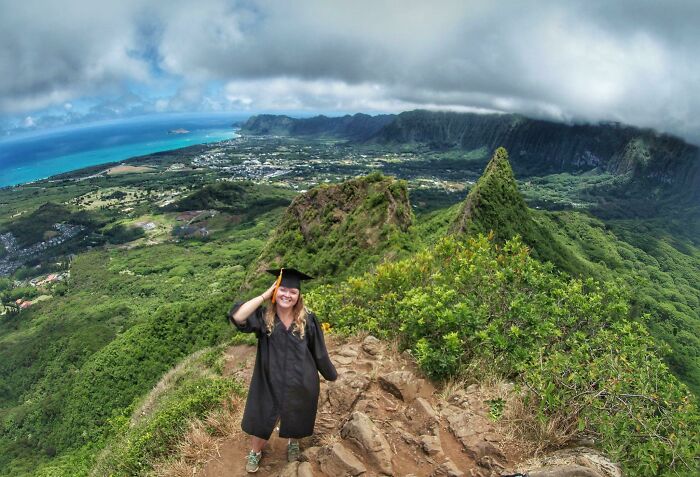 Woman in graduation gown on mountain peak overlooking lush landscape, symbolizing leap of faith and best life decisions.