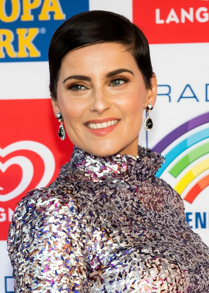 Nelly Furtado smiling at an event, wearing a shimmering sequin dress and dangling earrings.