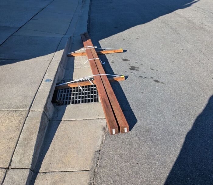 Wooden planks poorly blocking a street drain, illustrating jobs done so poorly it is almost impressive.