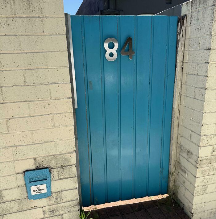 Blue gate with house number 84 mounted incorrectly, illustrating poor job e*******n almost impressive to see.