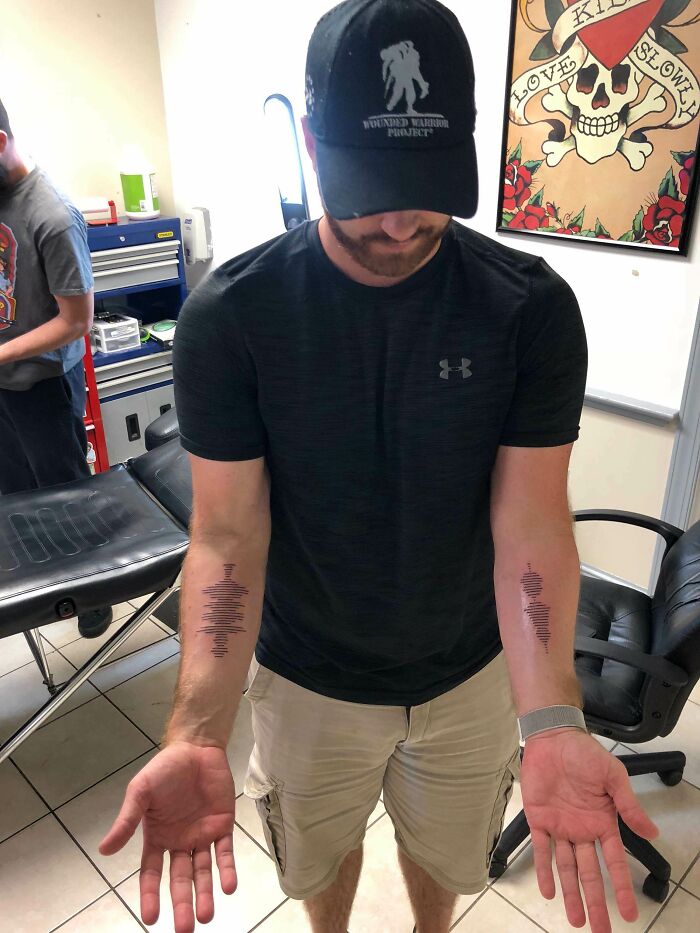 Man showing matching soundwave tattoos on both forearms in a tattoo studio, showcasing meaningful ink designs. Man showing matching soundwave tattoos on both forearms in a tattoo studio, showcasing meaningful ink designs.