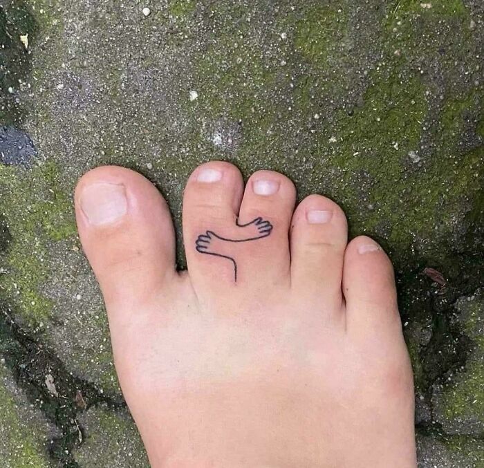 Minimalist toe tattoo of two small arms hugging, showcasing wholesome tattoos with meaningful little ink on foot.