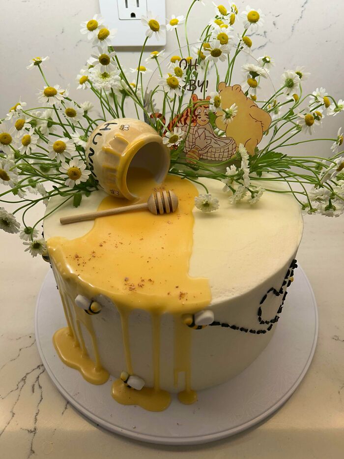 Honey-themed cake with dripping glaze, fresh flowers, and cartoon cake toppers showcasing masterful cake creativity.