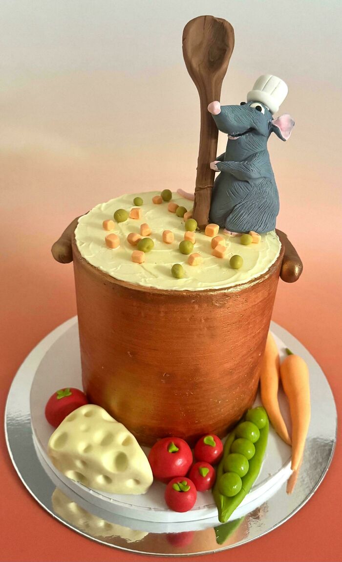 Masterfully crafted cake shaped like a soup pot with a chef mouse and detailed fondant vegetables on a reflective base.
