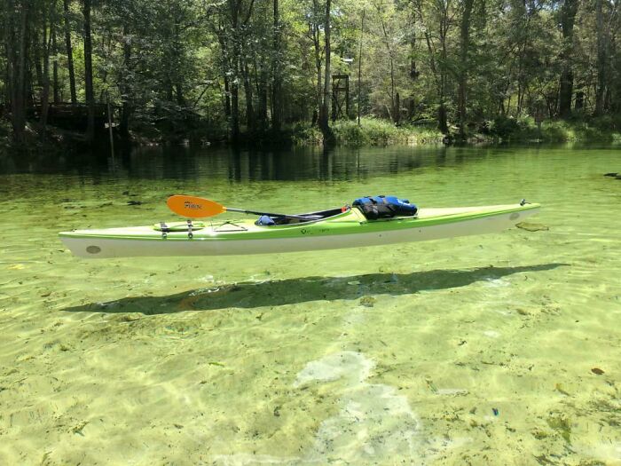 Green kayak appearing to hover above clear water in a forested area, a photo so confusing your brain might need a moment.