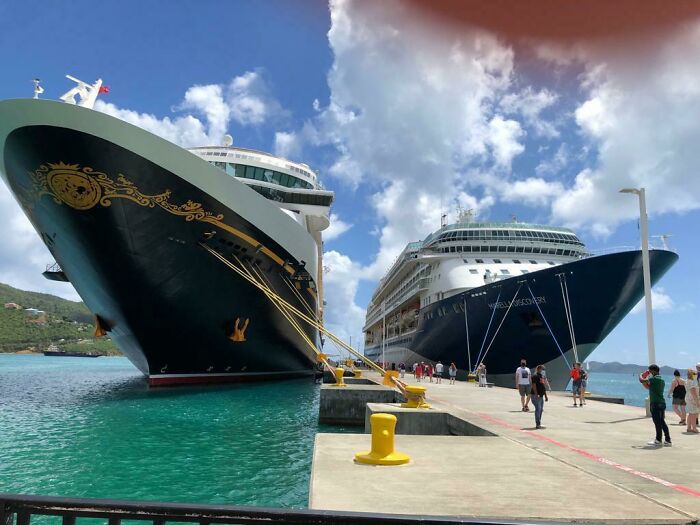 Two large cruise ships docked side by side at a pier with people walking nearby in a confusing visual scene.
